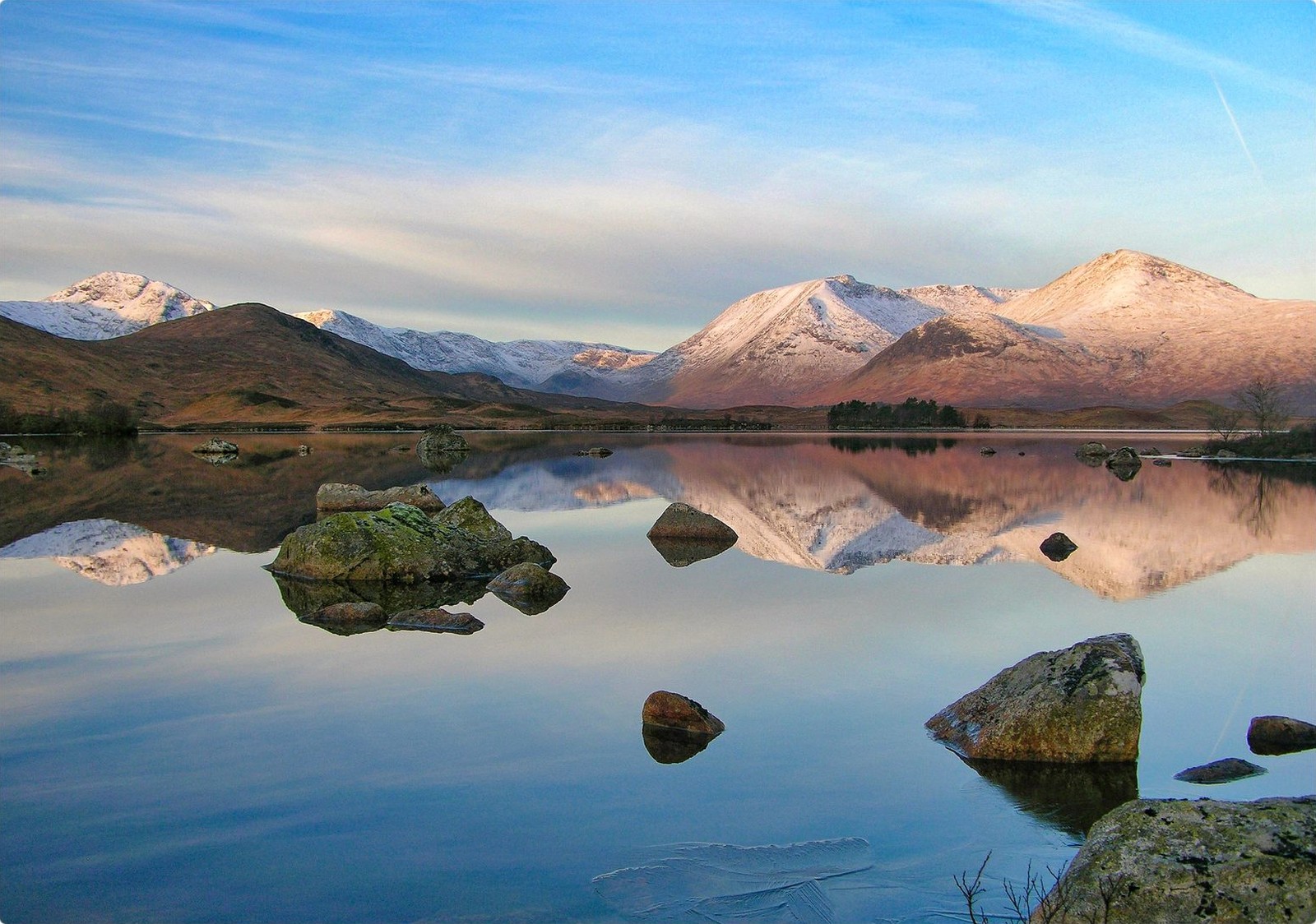 Snow-capped peaks glowing pink at first light, reflected in a still lochan on Rannoch Moor